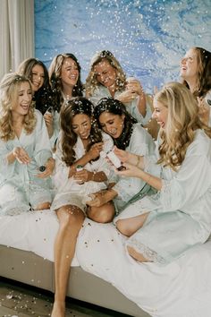 a group of women sitting on top of a bed in white robes and confetti