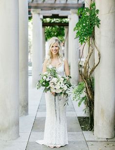 a woman in a white dress is holding a bouquet and standing on a sidewalk with columns