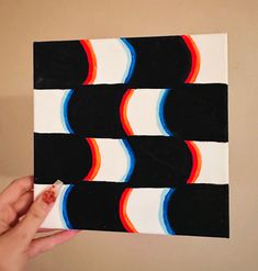 a hand holding up a piece of art with black, white and red stripes on it