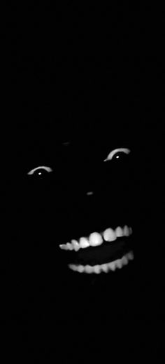 a black and white photo of the face of a person with glowing teeth in the dark