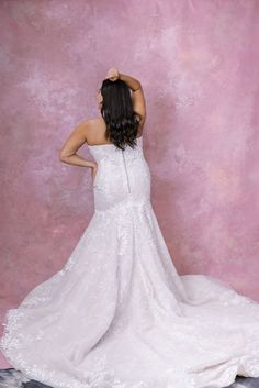 a woman in a white wedding dress standing against a pink wall with her back to the camera