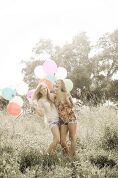 two young women walking through a field with balloons