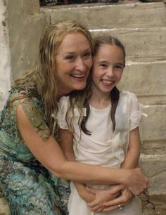 two girls are hugging each other in front of a brick wall and stone steps that lead up to the second floor