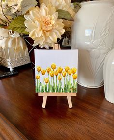 a card with yellow tulips on it sitting on a table next to white vases