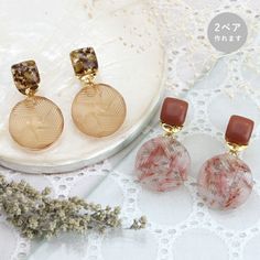 two pairs of earrings sitting on top of a white doily next to a flower