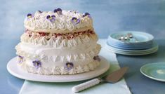 a cake with white frosting and purple flowers on it sitting on a plate next to plates