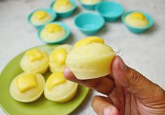 a hand holding a piece of yellow cake next to some blue and green cupcakes