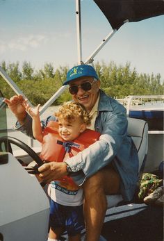 an older man is holding a young boy in his arms while sitting on a boat