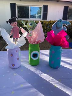 three vases with paper monsters in them sitting on a table near a house and bushes