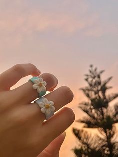 a person's hand with two flower rings on it, and the sky in the background