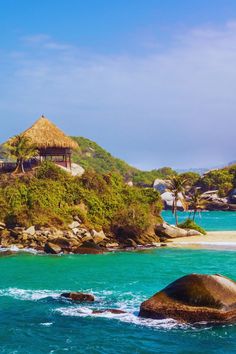 an island with a thatched hut on top in the middle of blue water and rocks