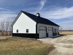 a large white barn with a black roof and two garage doors on the side of it