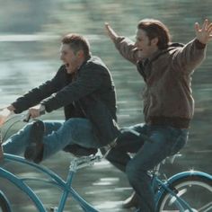 two men riding bikes in the rain with their arms up and one holding his hand out