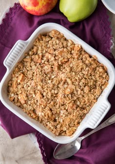 a casserole dish filled with oatmeal next to apples and spoons