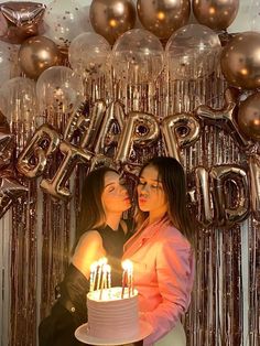 two women standing next to each other in front of a cake with candles on it