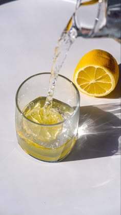 a glass filled with water next to an orange and a lemon on a white table