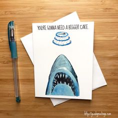 there is a card with a shark on it and a pen sitting next to it