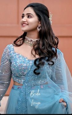 a woman with long hair wearing a blue dress and jewelry is smiling at the camera