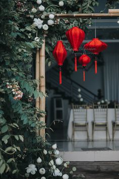 three red lanterns hanging from a trellis in front of a table with white flowers