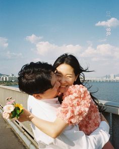 two women hugging each other on a bridge over looking the water with buildings in the background