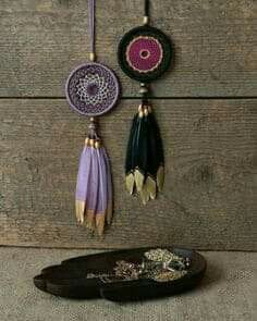 three pieces of jewelry hanging on a wooden wall next to a tray with beads and chains