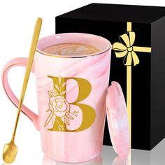 a pink marbled coffee mug next to a black box and gold spoon with a golden b on it