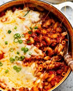 a large pot filled with pasta and meat covered in sauce, cheese and green onions