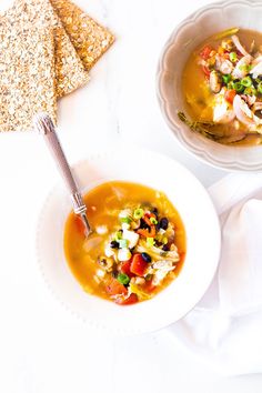 two bowls filled with soup next to some crackers on the side and napkins