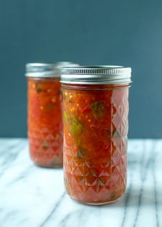 two jars filled with food sitting on top of a white marble counter next to each other