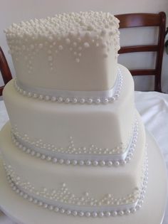 a three tiered white wedding cake with pearls