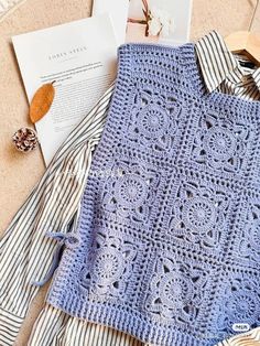 a blue crocheted sweater sitting on top of a bed next to an open book