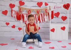 a little boy sitting on a chair in front of some red hearts