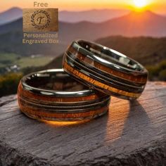 two wedding bands with wood inlays are sitting on a rock at sunset, overlooking the mountains