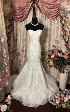 a white wedding dress on display in front of floral wallpaper and curtained window