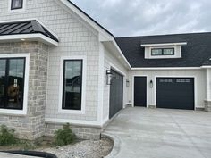 a white house with black garage doors on the front and side windows in gray brick