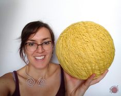 a woman holding up a ball of yarn in front of her face and smiling at the camera