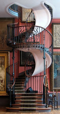 a spiral staircase in an old house with paintings on the walls and wooden flooring