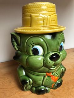 a green ceramic animal with a yellow hat on it's head sitting on a wooden table