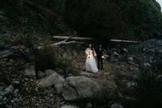 a bride and groom standing on the side of a rocky hill at night with their arms around each other