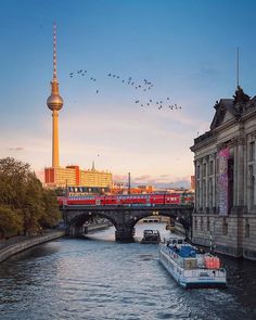 a boat traveling down a river next to a tall building with a tv tower in the background