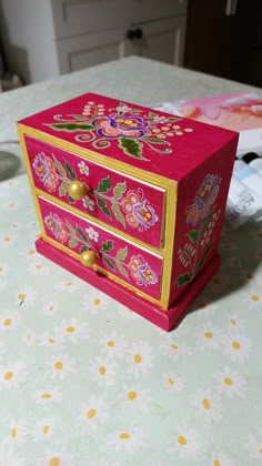 a pink and gold decorated box sitting on top of a white tablecloth covered table