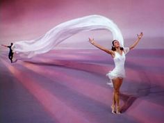 a woman in a white dress is dancing with her arms spread out and hands are outstretched