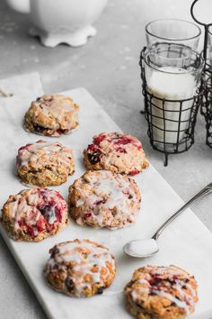 a white plate topped with muffins covered in icing next to a glass of milk