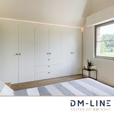 a bedroom with white cabinets and a large bed in front of two windows that overlook the countryside