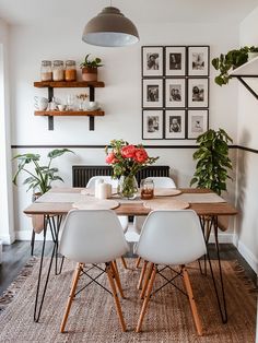 a dining room table with white chairs and pictures on the wall above it, along with potted plants