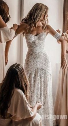 two women in dresses are helping another woman put on her wedding dress