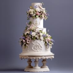 a three tiered white wedding cake with flowers on the top and sides, against a gray background