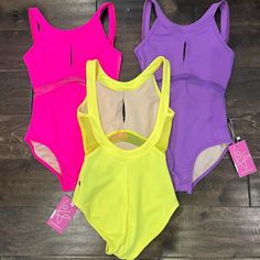 three women's swimsuits sitting on top of a wooden floor next to each other