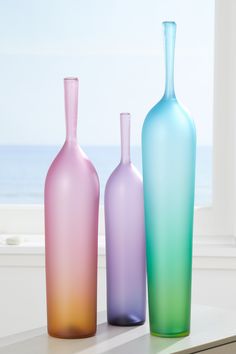 three different colored vases sitting next to each other on a window sill near the ocean