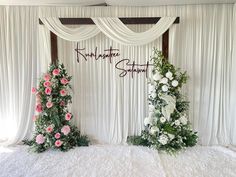 two floral arrangements are on the bed in front of white drapes with writing and flowers